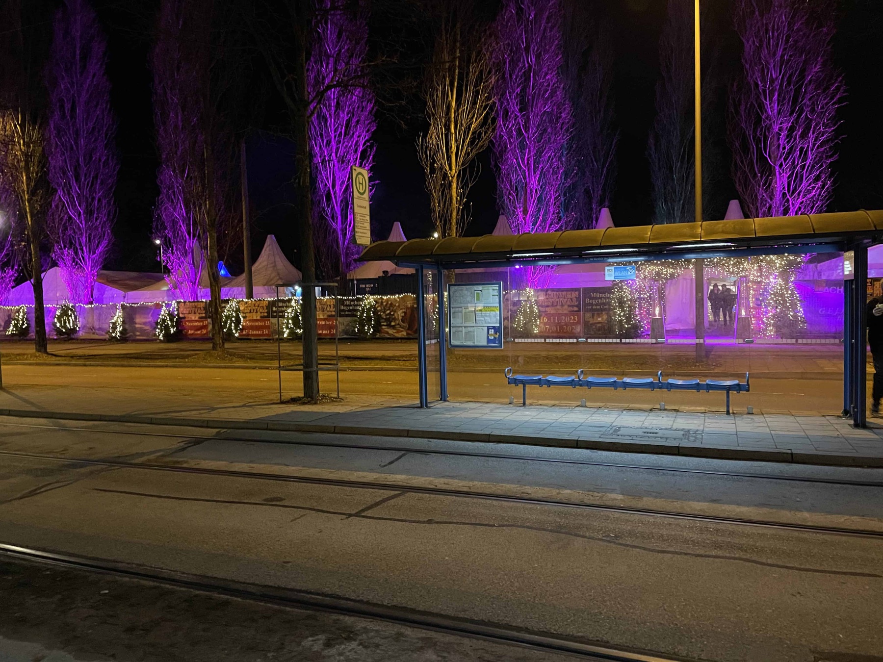 Nächtliche Straßenszene in Bogenhausen: violett beleuchtete Bäume und Lichterketten über den Marktständen